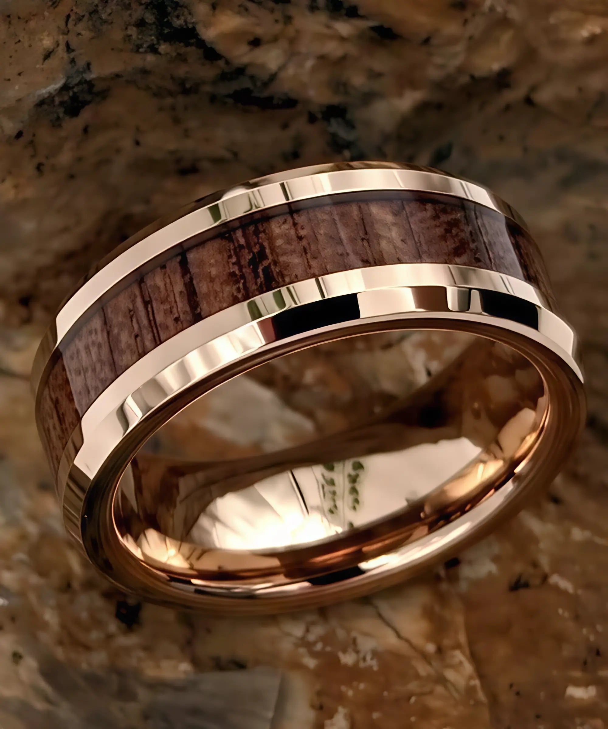 Bague en bois de koa et tungstène or rose, posée sur une pierre naturelle aux reflets bruns.